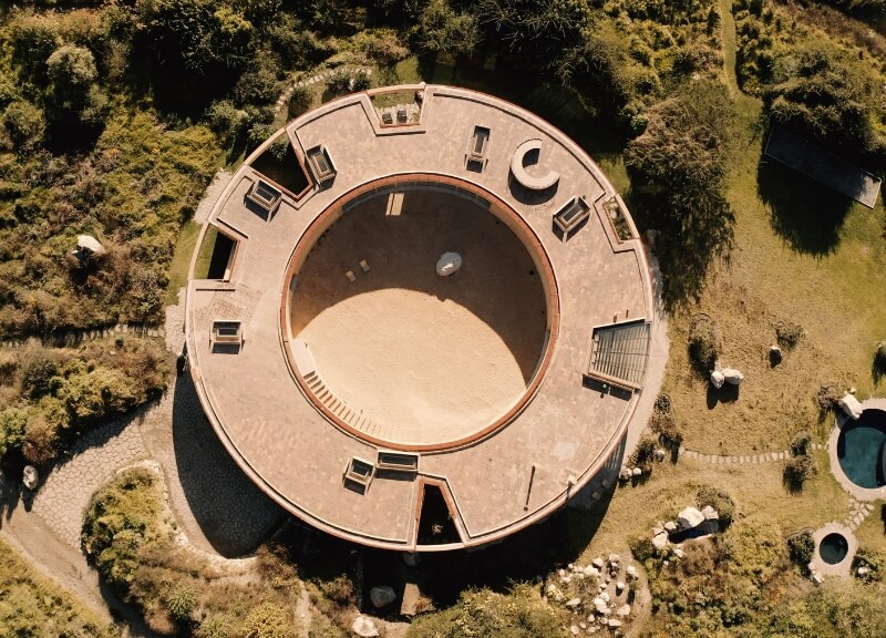 Top-down drone view of Casa 720 revealing its circular plan nestled in forest and lake.