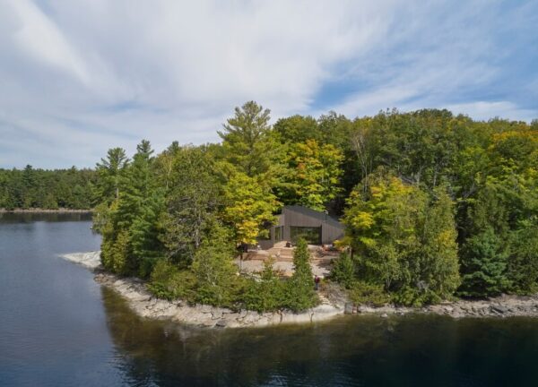 Aerial view of Catchacoma Cottage hovering above the wooded lakeshore, revealing roof volumes.